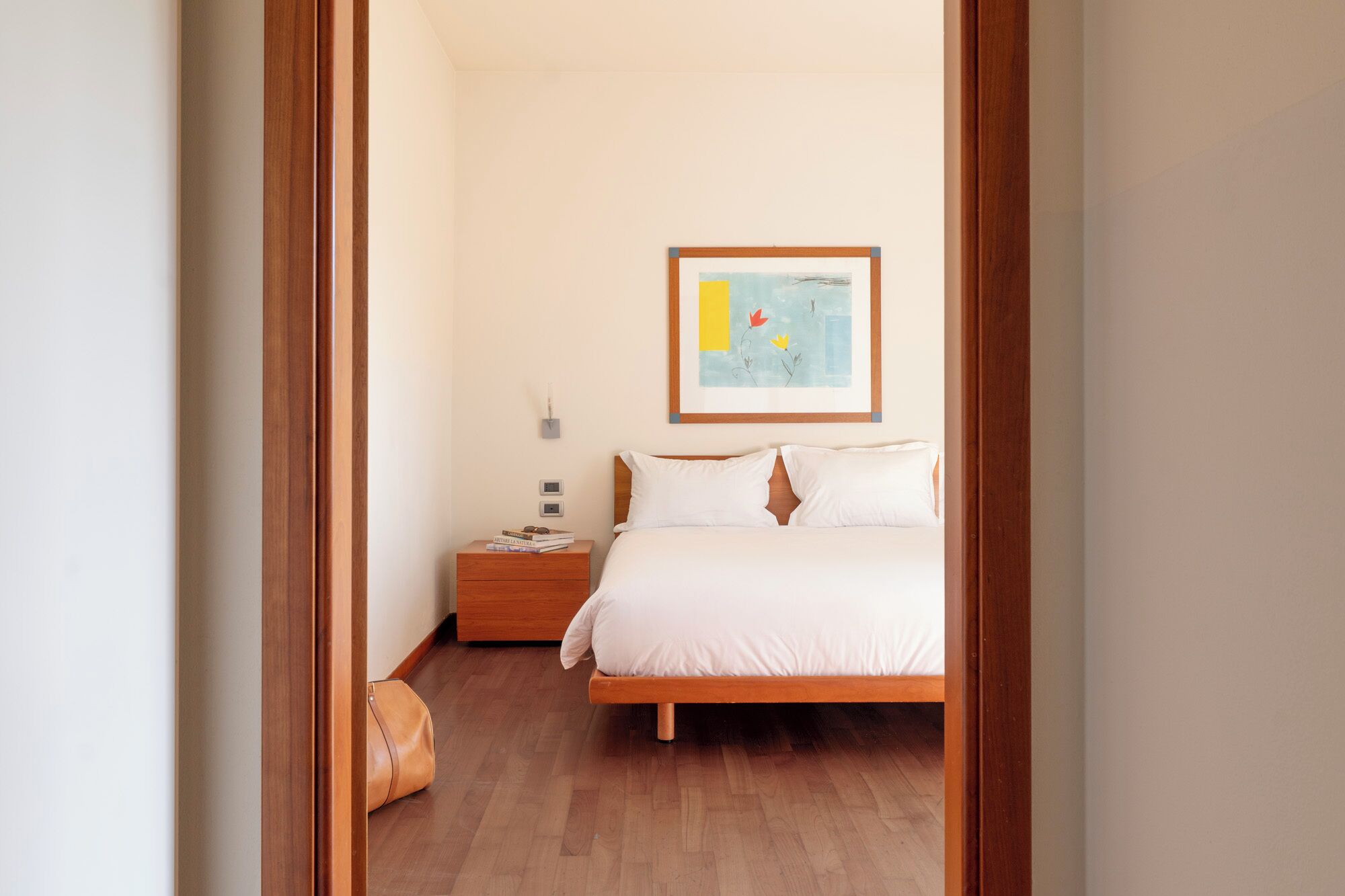 Une chambre à coucher comprenant un lit, une table de chevet, une œuvre d’art accrochée au mur et un plancher en bois.