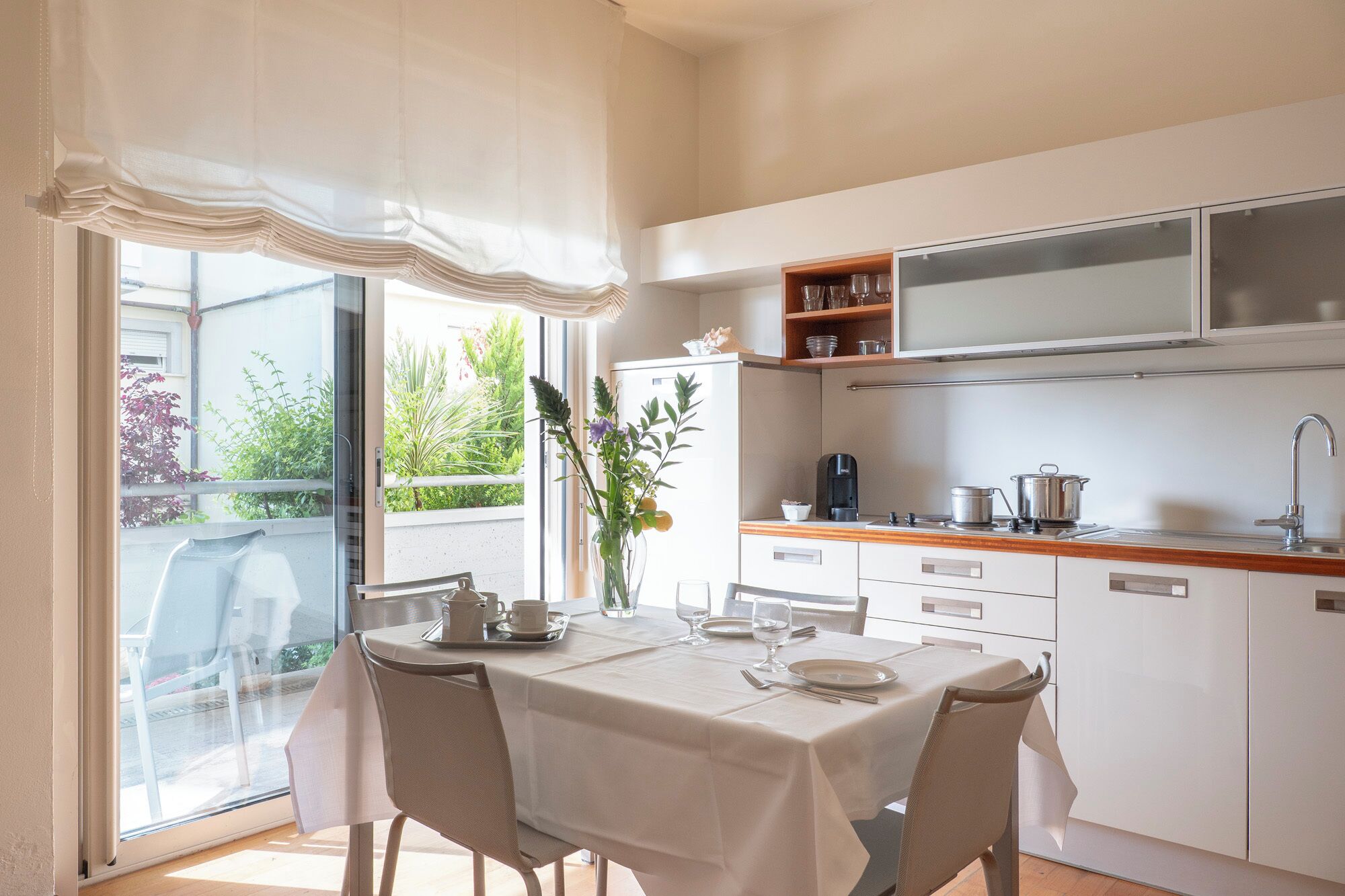 Une cuisine moderne avec des meubles blancs, une table à manger dressée pour deux personnes et une vue sur la verdure à l’extérieur.