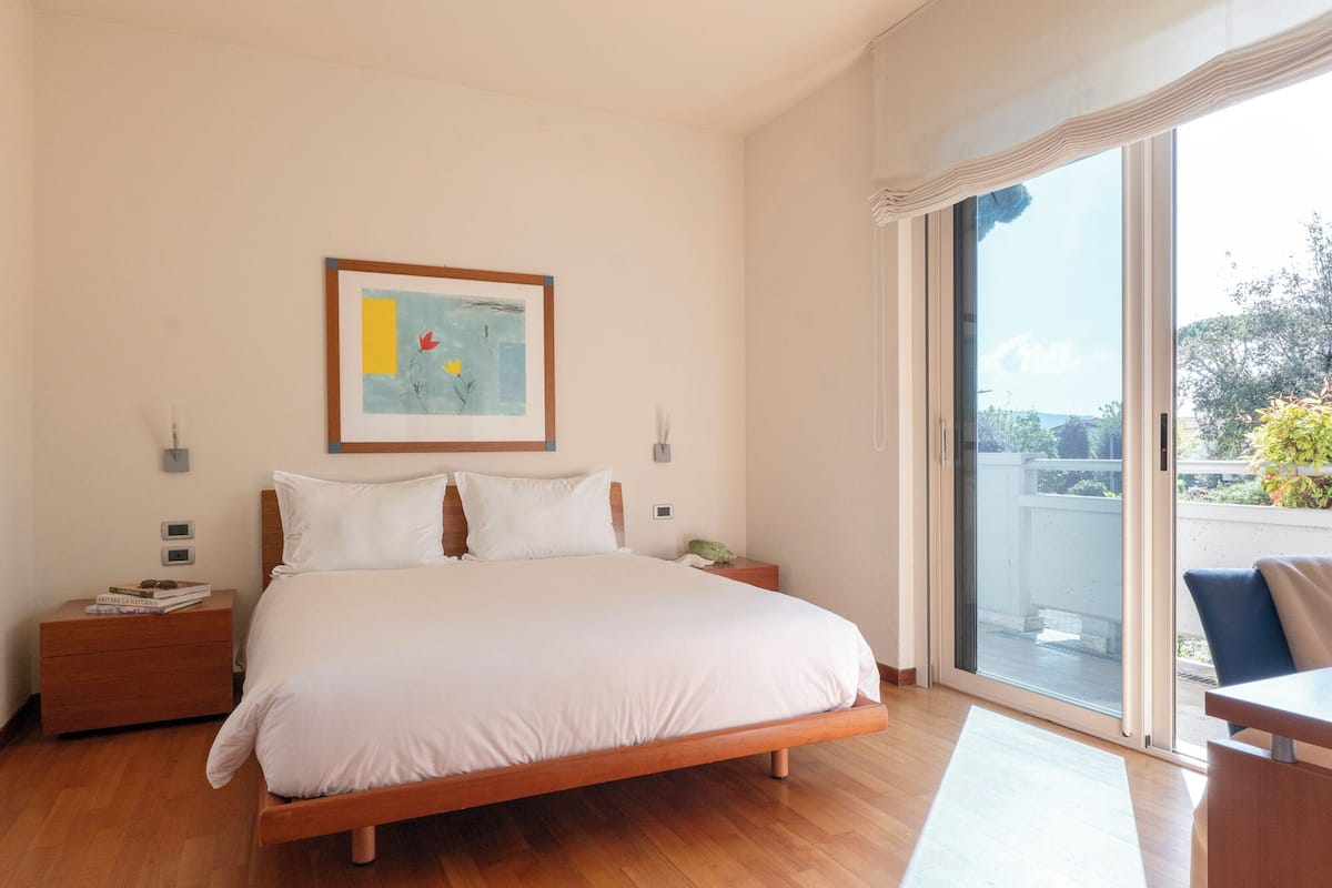 Una camera da letto con un letto, comodini, un'opera d'arte appesa al muro e vista tramite una porta scorrevole in vetro.