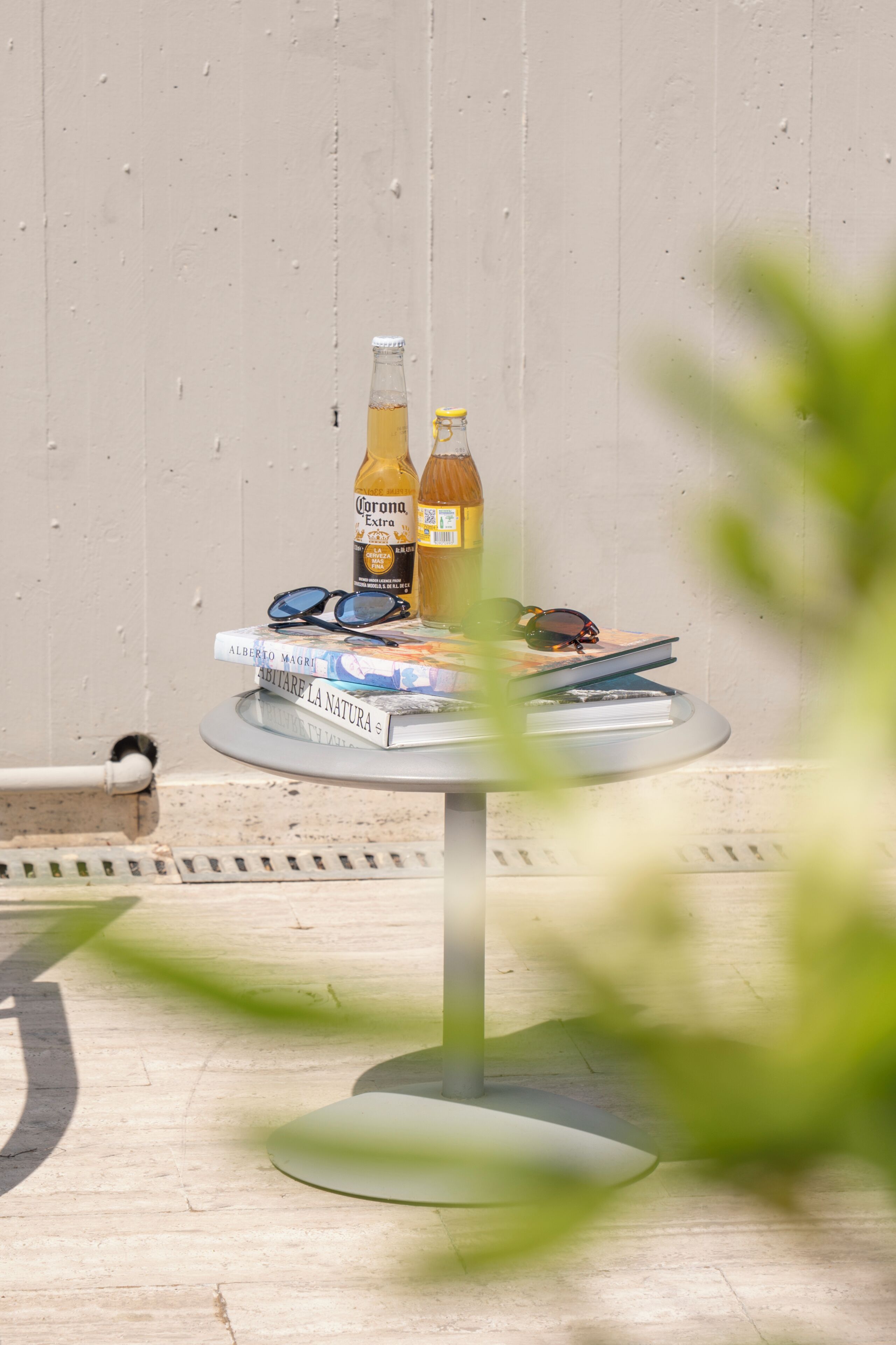 Una mesa redonda con libros, dos botellas y gafas de sol.