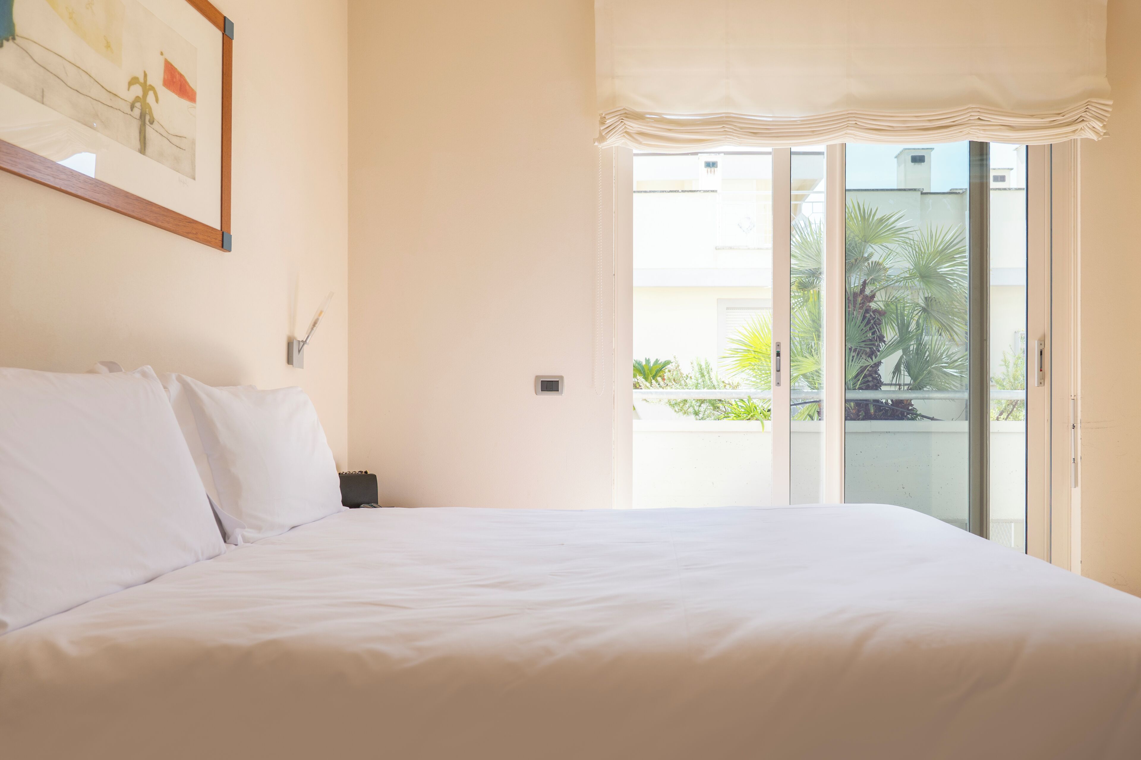 A bedroom with a large bed, a sliding glass door to a balcony, and a framed picture on the wall.