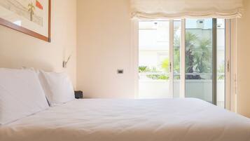 A bedroom with a large bed, a sliding glass door to a balcony, and a framed picture on the wall.