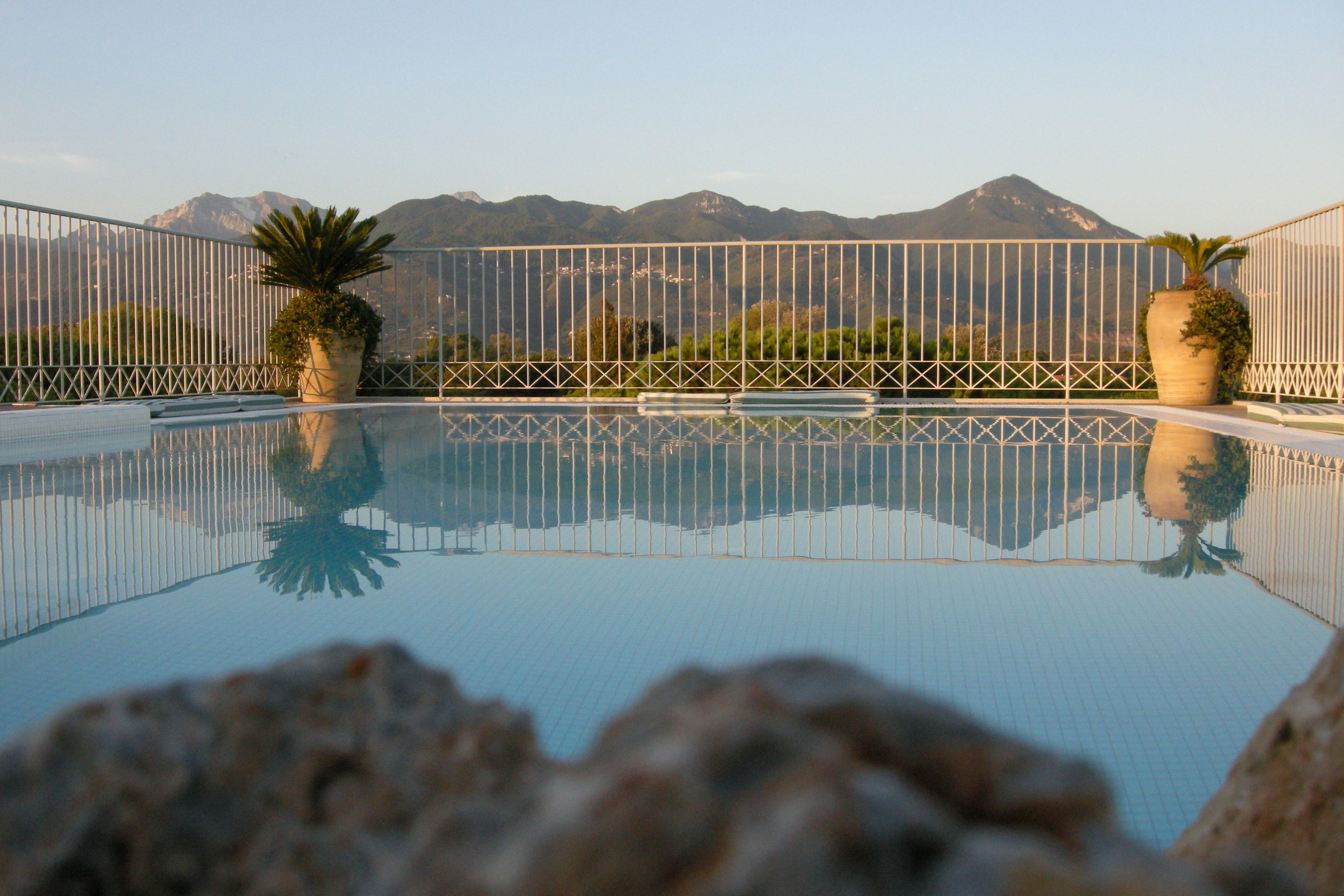 Piscina cristalina con vistas a montañas al fondo, rodeada por una cerca blanca.