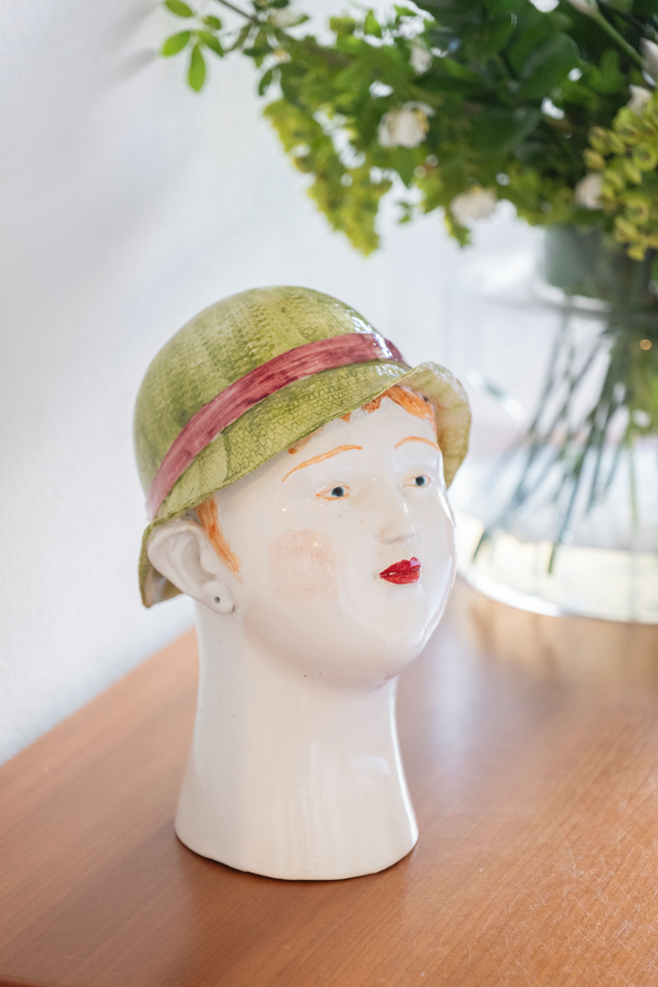 A ceramic bust with a hat on a wooden surface.