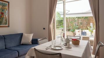 A dining area with a table set for two, a blue sofa, and a view of a garden through a glass door.
