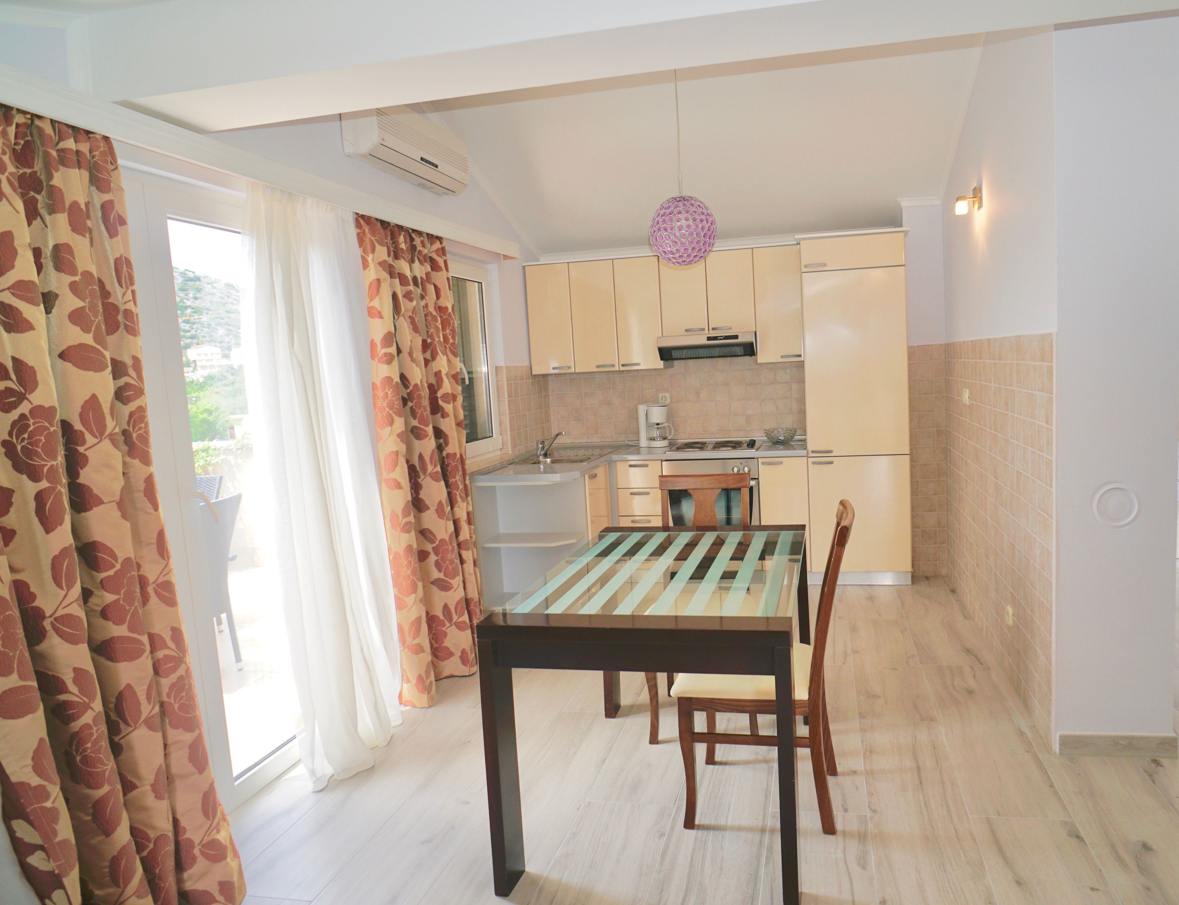 A compact kitchen with a dining table and chairs, a coffee machine, and a hanging light fixture.