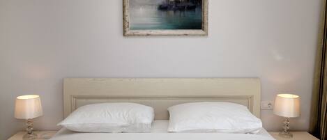 A neatly made bed with white linens, two bedside tables with lamps, and a framed painting on the wall.