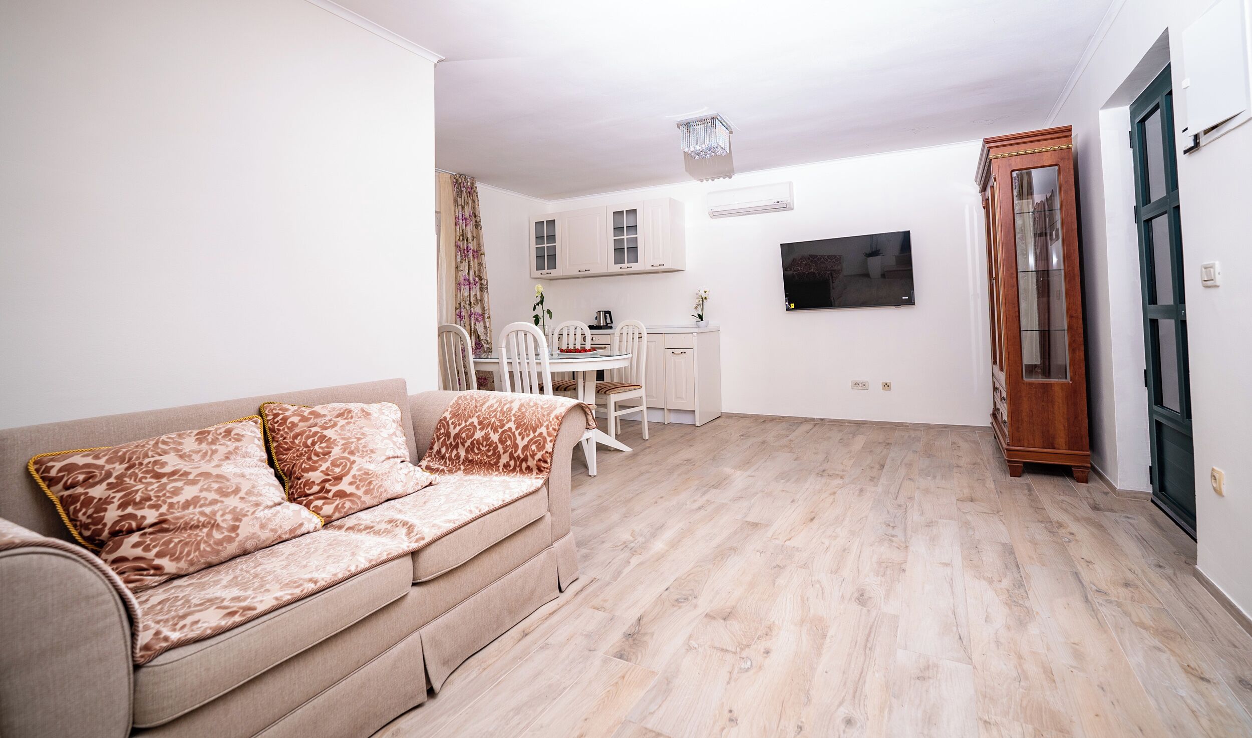 Una sala de estar con sofá y sillones, un comedor con mesa y sillas, una cocina con armarios y un televisor, y una puerta de madera.