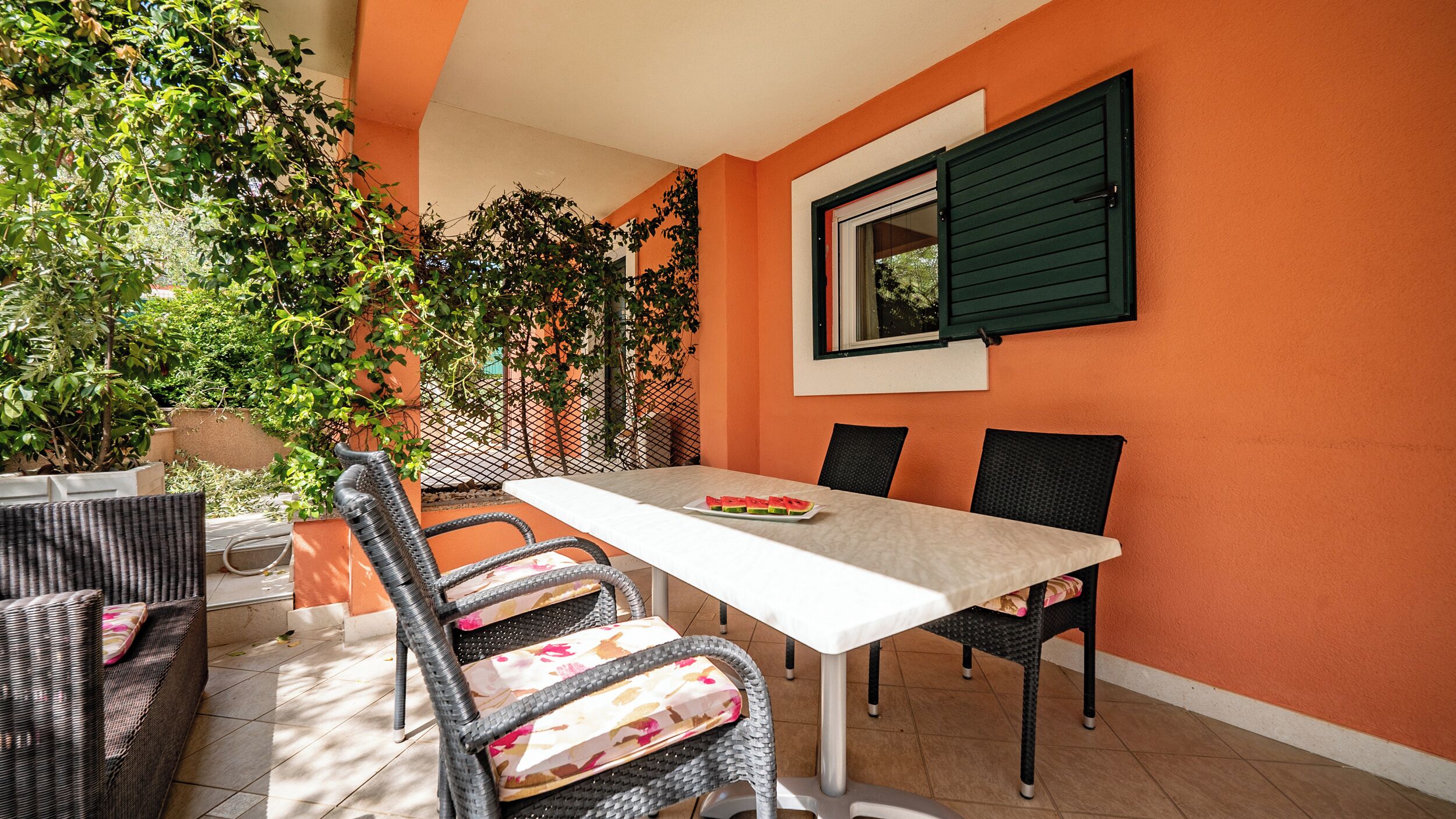An outdoor patio with a table and chairs, surrounded by orange walls and greenery.