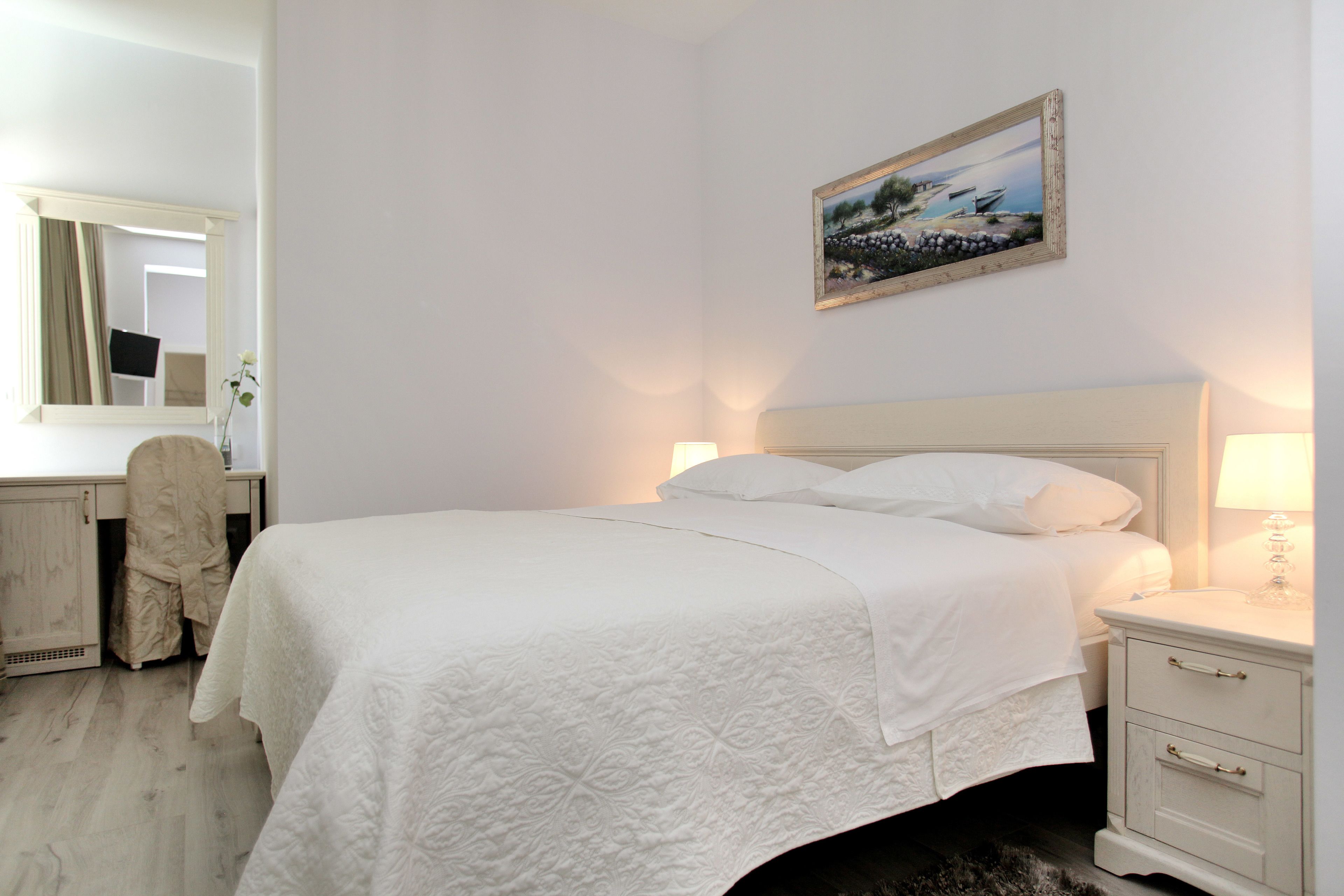 A neatly arranged bedroom with a bed, bedside tables, a chair, a mirror, and a painting on the wall.