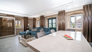 A modern living room with a blue sofa, a glass coffee table, and a dining table with a watermelon slice.