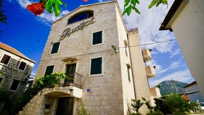 A building with the name 'Justica' on the facade, featuring a stone exterior, a balcony with plants, and a clear blue sky in the background.