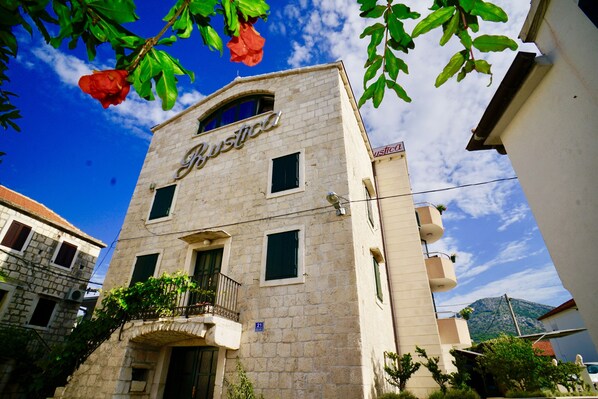 A building with the name 'Justica' on the facade, featuring a stone exterior, a balcony with plants, and a clear blue sky in the background. - Villa Rustica Dalmatia Apartments (Seget)
