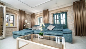 A living room with a blue sofa, a glass coffee table, and a view of a stone wall and a green door.