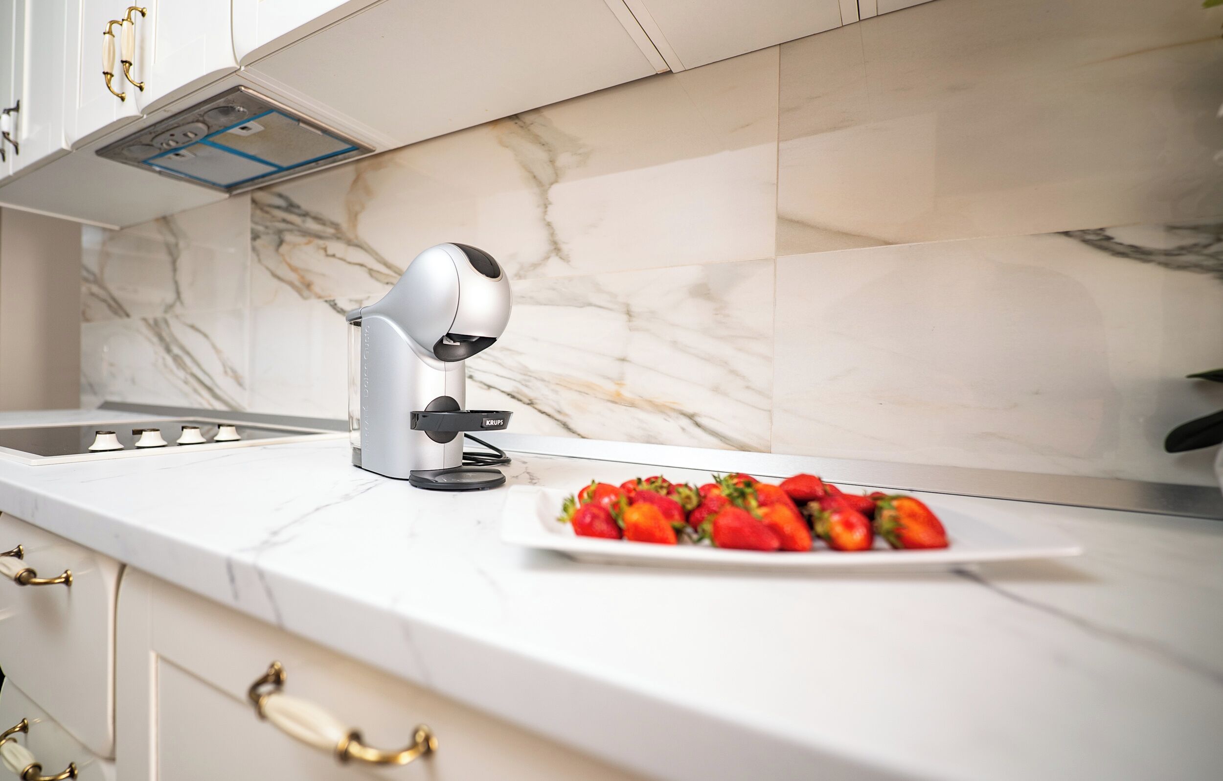 A modern kitchen with a marble backsplash, a built-in oven, and a plate of strawberries on the counter.