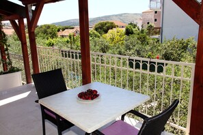 A balcony with a table and chairs, a bowl of cherries, and a view of greenery and buildings in the background. - Villa Rustica Dalmatia Apartments (Seget)