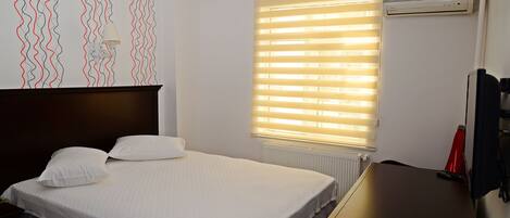 A hotel room with a bed, a desk, a radiator, and a window with blinds.