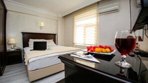 Habitación de hotel con cama, mesita de noche y una bandeja de frutas con una copa de vino tinto.