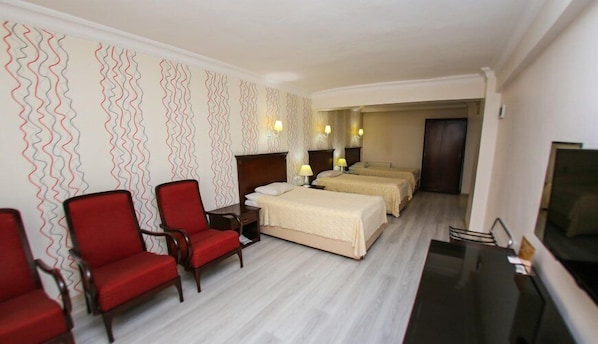 A hotel room with a bed, two bedside tables with lamps, a TV, and two red chairs. - Hotel Sahiner (Nigde)