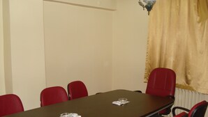 Un salón de conferencias con una larga mesa, sillas rojas y una araña.