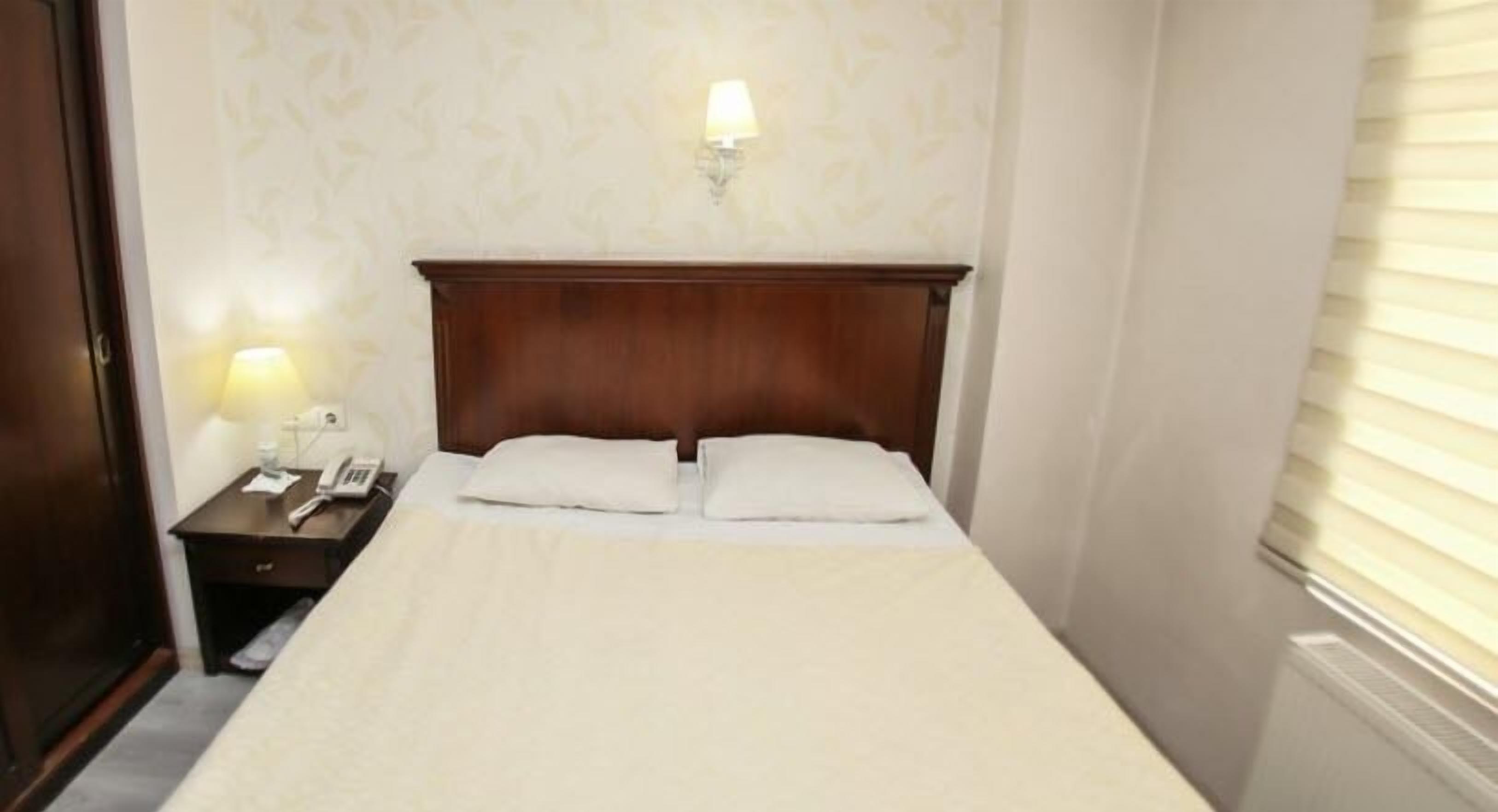 Una habitación de hotel con cabecera de madera, una mesita de noche con lámpara y teléfono.