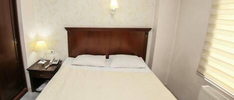 Una habitación de hotel con cabecera de madera, una mesita de noche con lámpara y teléfono.