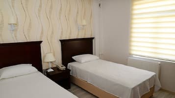 Una habitación de hotel con dos camas individuales, una mesita de noche con lámpara y una ventana con persianas.