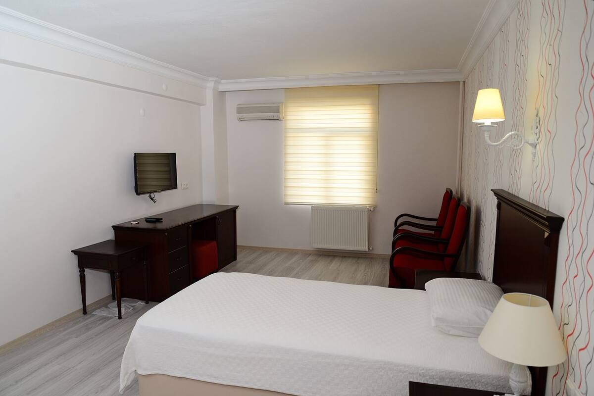 A hotel room with a bed, a desk, a chair, a TV, and a window with blinds.