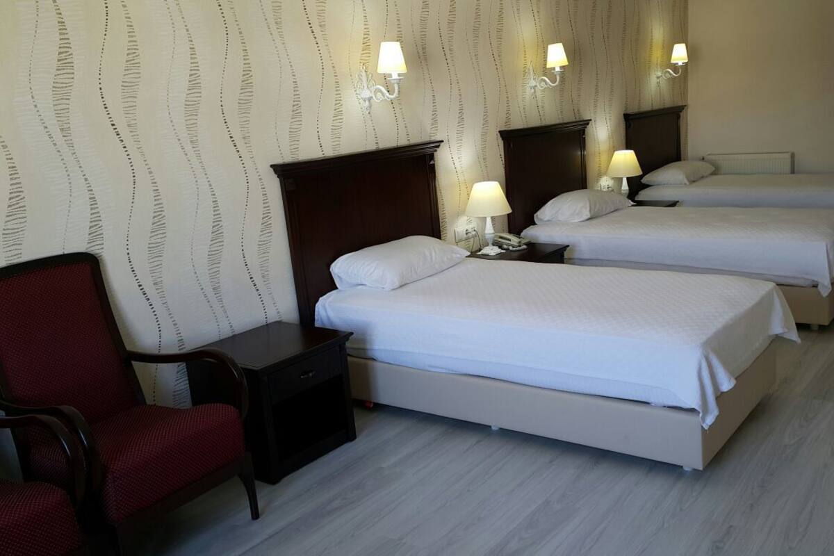 A hotel room with three beds, a red armchair, a bedside table with a lamp, and a wall-mounted telephone.