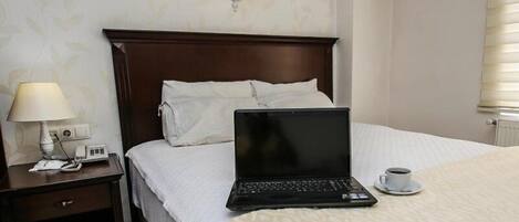 Una habitación de hotel con una cama, una mesita de noche con una lámpara, una computadora portátil y una taza de café sobre la cama.