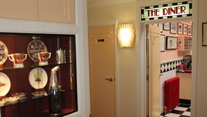 A hallway with a glass display case containing plates and a bottle, a door labeled "THE DINER", and a checkered floor. - The PitStop (Bishop's Stortford)