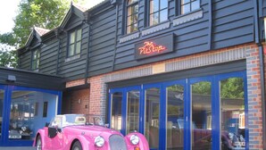 A vintage pink convertible car parked in front of a building with a neon sign reading "The Place Inn." - The PitStop (Bishop's Stortford)