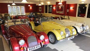 A vintage car showroom with multiple classic cars on display. - The PitStop (Bishop's Stortford)