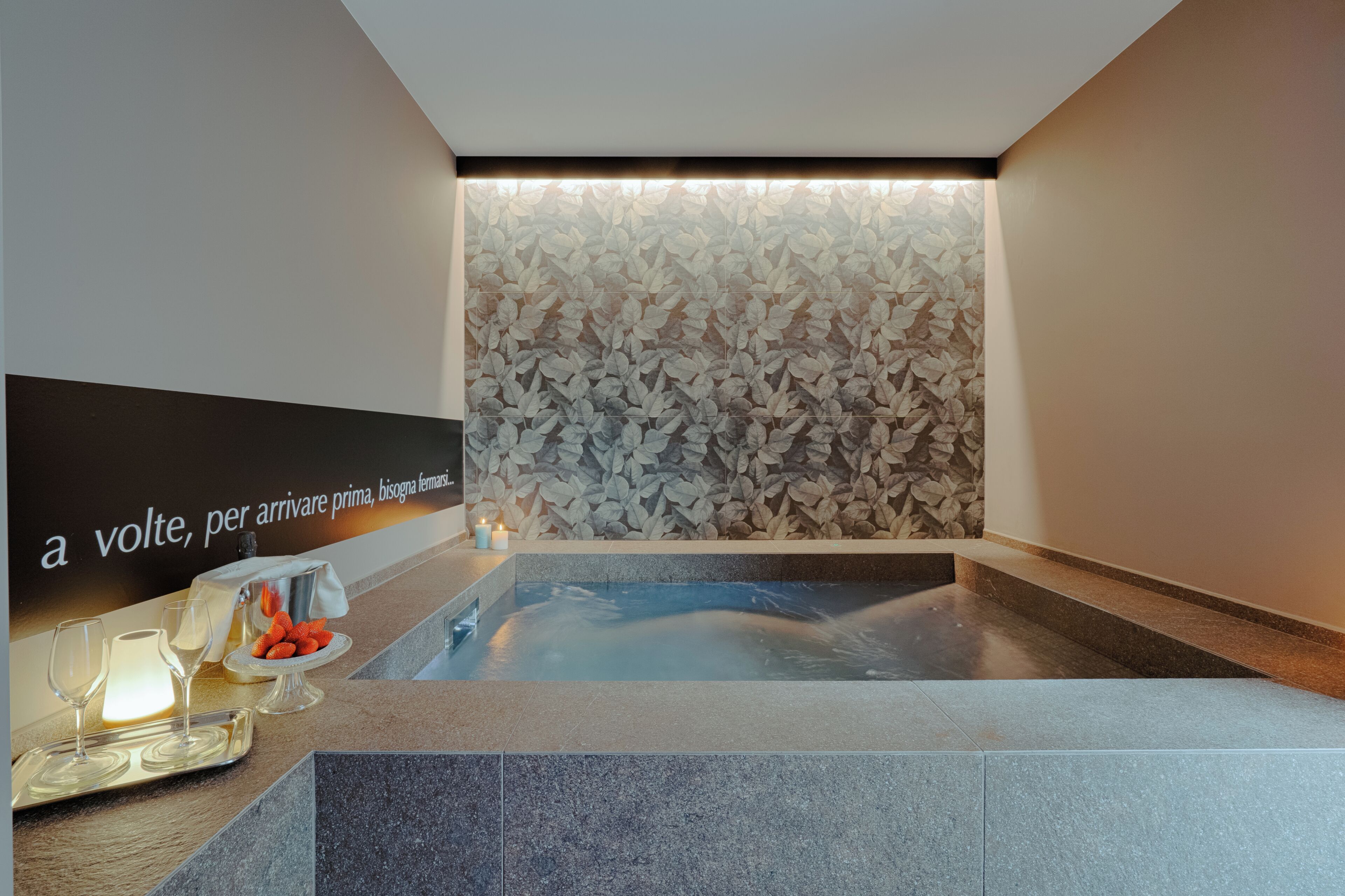 A spa area with a hot tub, a wall with a leaf pattern, and a counter with glasses and snacks.