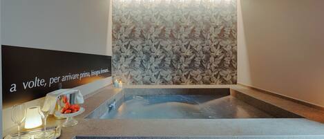 A spa area with a hot tub, a wall with a leaf pattern, and a counter with glasses and snacks.