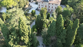 An aerial view of a large building surrounded by dense trees, with a parking area and a small garden.
