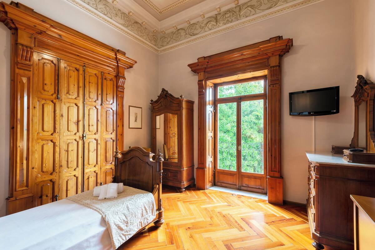 Une chambre avec une armoire en bois, un lit, une commode et un téléviseur fixé au mur.