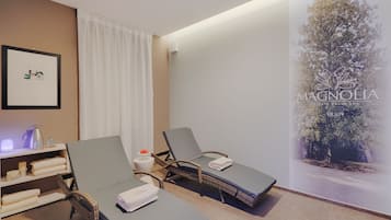 Un cuarto de spa con dos sillones reclinables, una repisa con toallas, un cuadro enmarco y una pared con un árbol y texto.