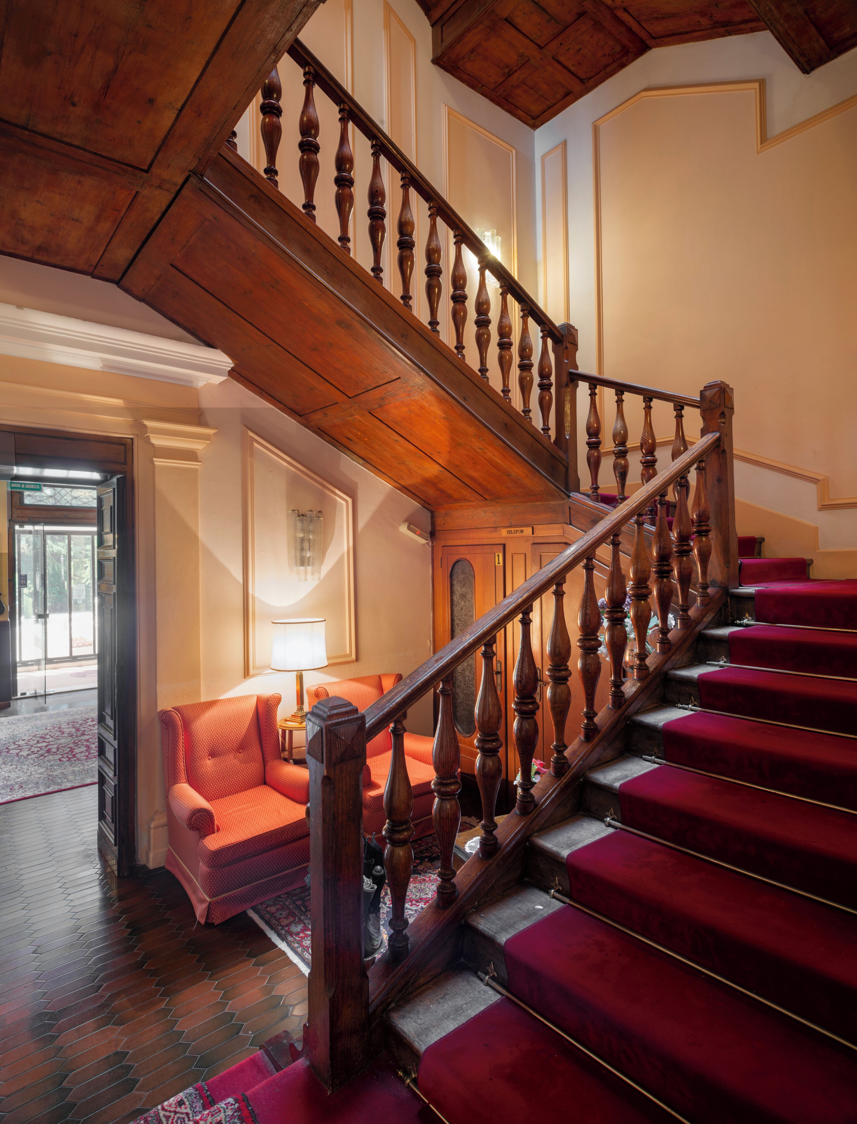 A staircase with wooden balusters and red carpeted steps leading to a landing.