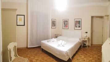 Habitación de hotel con cama, mesita de noche y una silla. Se observan cuadros en la pared y una puerta a la derecha.
