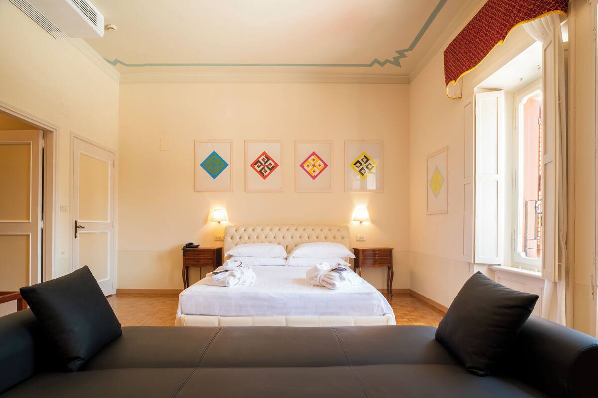 Une chambre d’hôtel avec un grand lit, deux tables de chevet, un canapé et une fenêtre avec des rideaux.