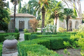 A garden with a building featuring arched windows and a tiled roof. - Villa Quiete (Montecassiano)