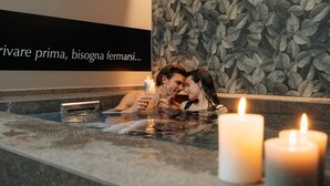 A couple in a hot tub with candles, a wall with a leaf pattern, and a sign with text. - Villa Quiete (Montecassiano)