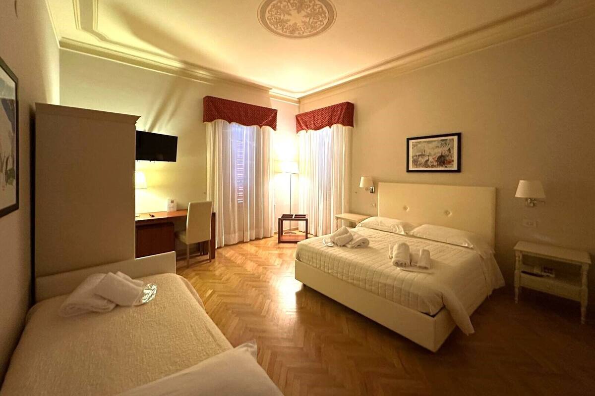 Une chambre d’hôtel avec deux lits, un bureau, une chaise, une petite table et un tableau au mur.