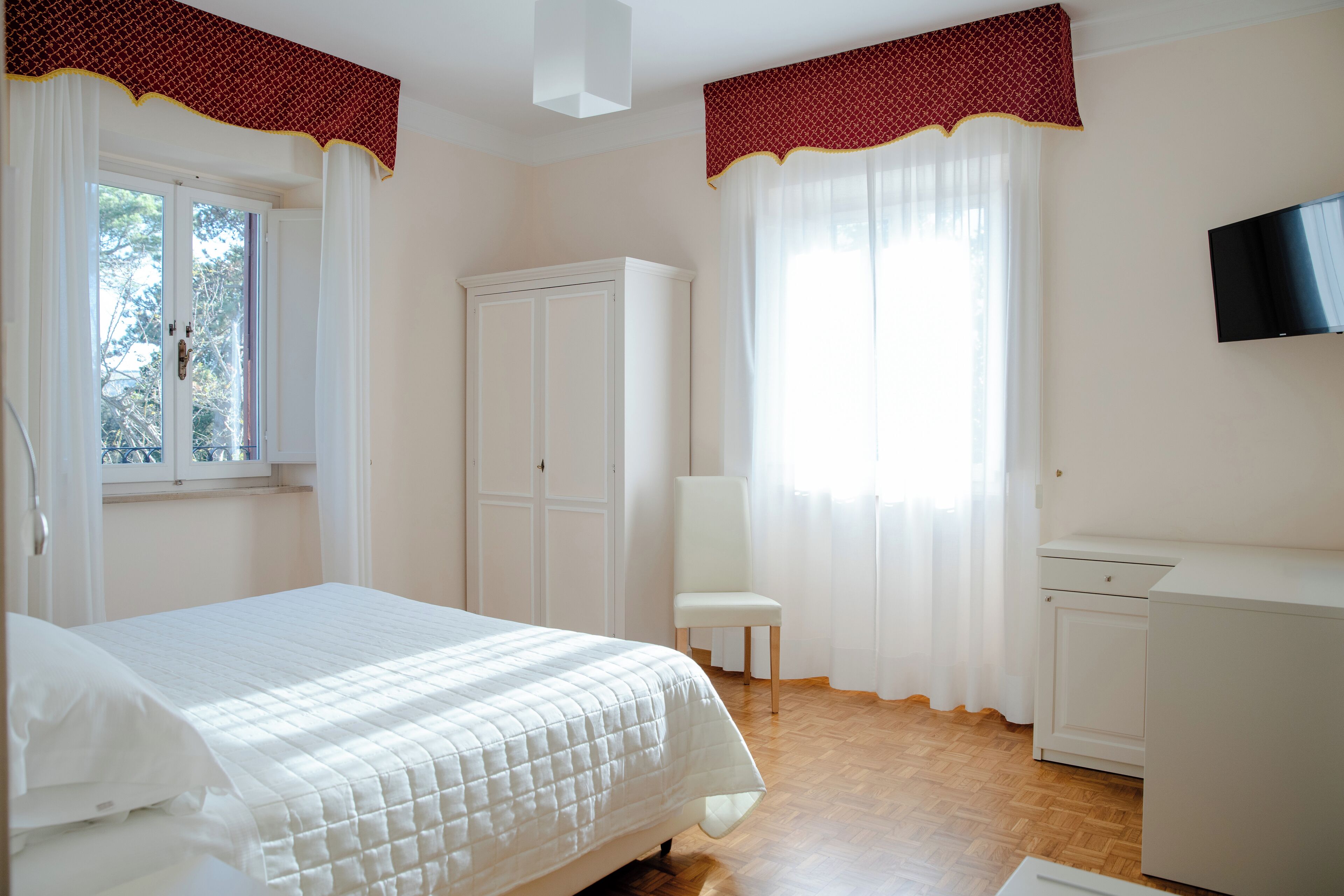 Un dormitorio con cama, una silla, armario, televisor y ventana con cortinas.