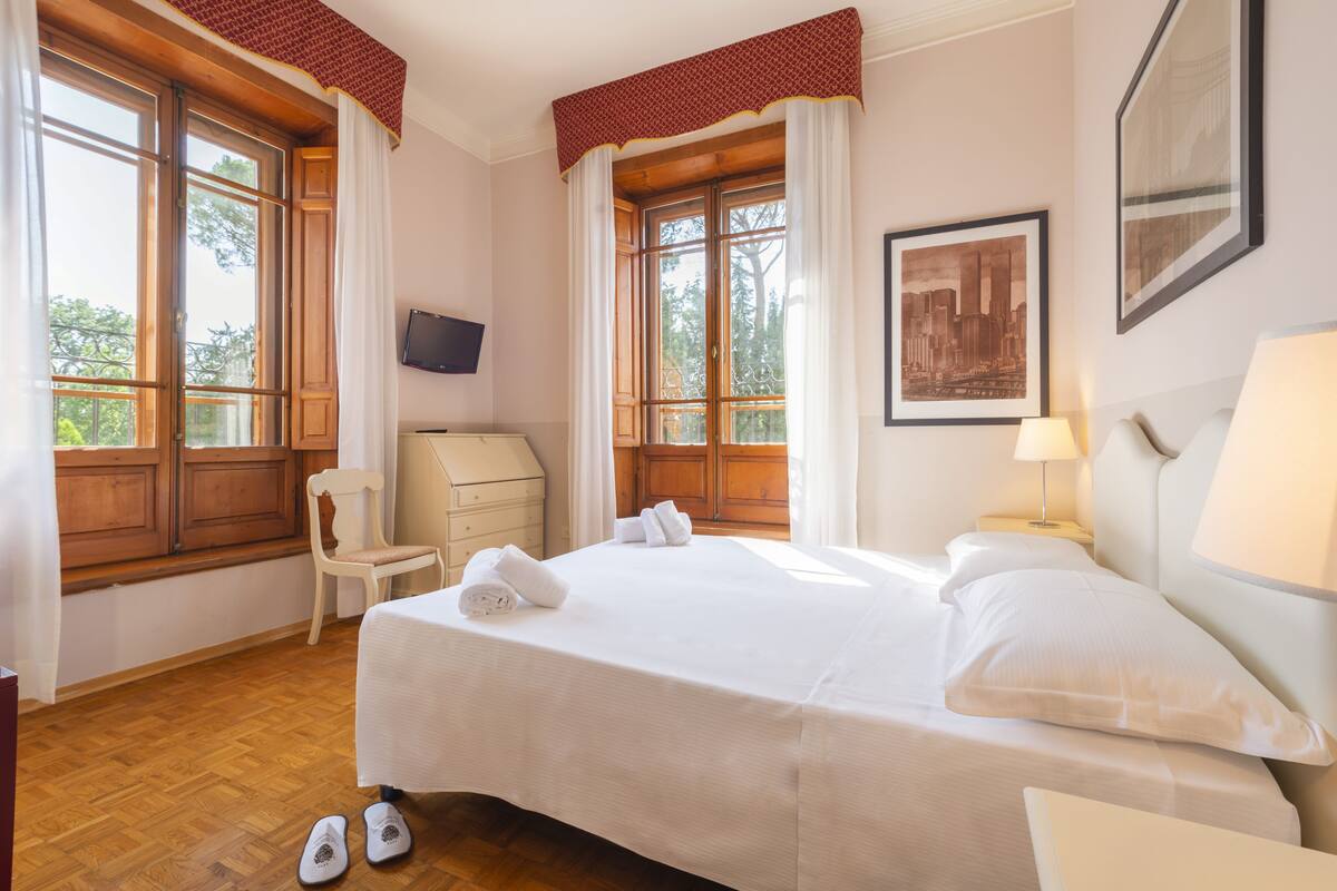 Une chambre d’hôtel avec un grand lit, une chaise, un bureau et une fenêtre avec des rideaux.