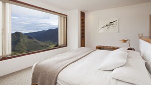 A bedroom with a large window, a bed, a bedside table, a lamp, and a wall-mounted artwork. - Hotel El Crater (San Antonio de Pichincha)