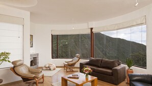 A spacious living room with a large window offering a mountain view, a brown leather sofa, a beige leather chair, and a wooden coffee table. - Hotel El Crater (San Antonio de Pichincha)
