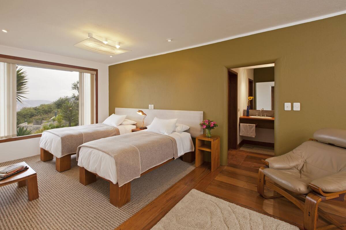 A modern bedroom with two beds, a wooden floor, a small table, and a view of the outdoors.
