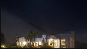 A modern building with multiple illuminated rooms, surrounded by cacti and palm trees, under a starry night sky. - Hotel El Crater (San Antonio de Pichincha)